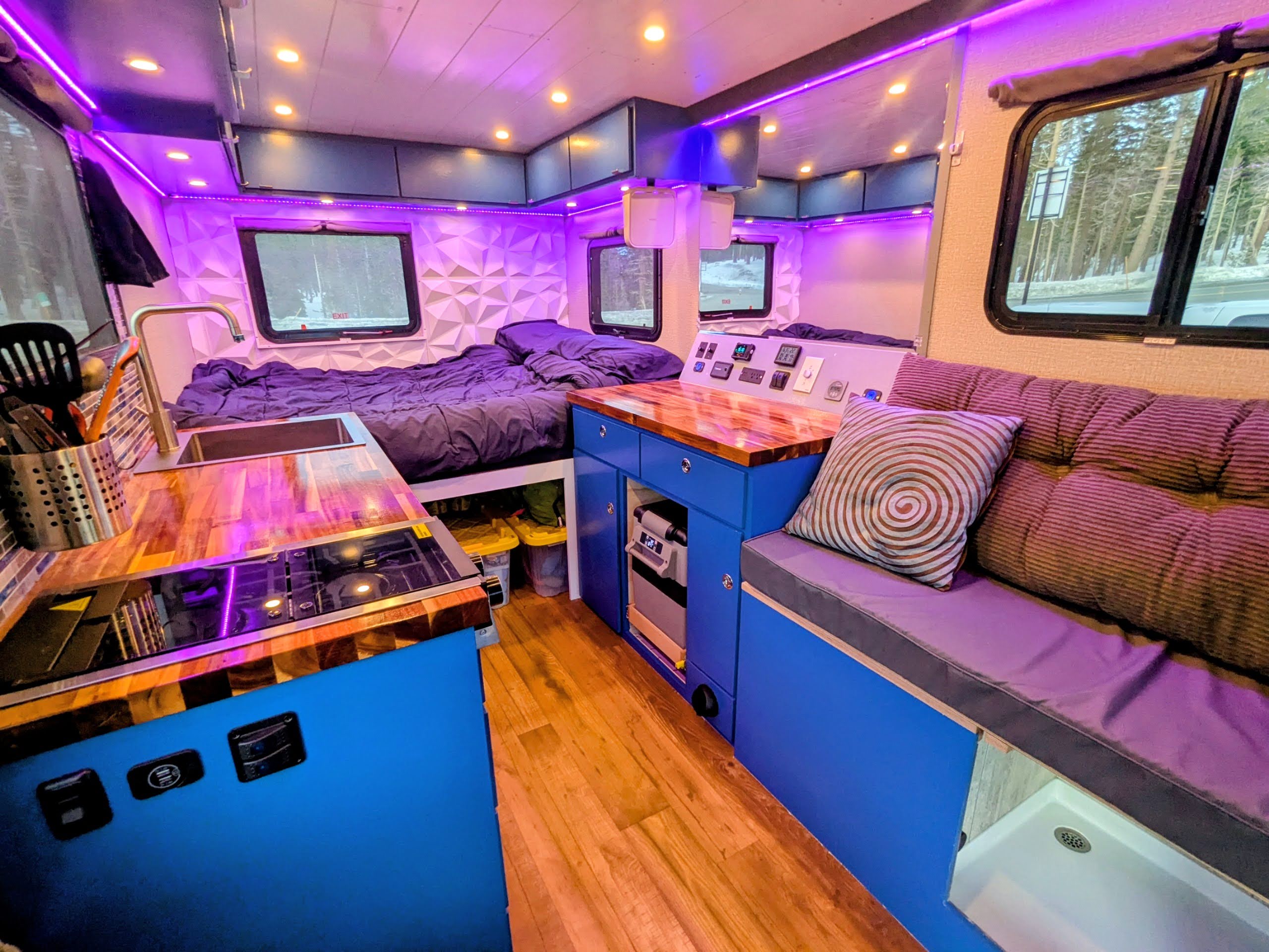 Full interior of custom ski van — kitchen, couch, and bed with ambient lighting